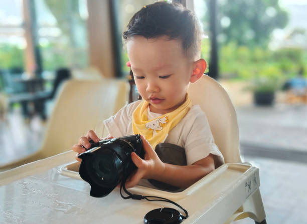 The boy hold a digital camera in his hand while smiling slightly.