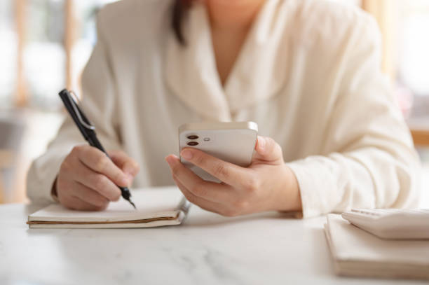 istock A cropped image of a woman writing something in her notebook and using her smartphone. 2158194290