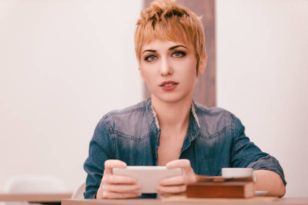 Profile view of aged 20-29 years old who is beautiful caucasian female standing in front of white background wearing jeans who is smiling and using mobile phone