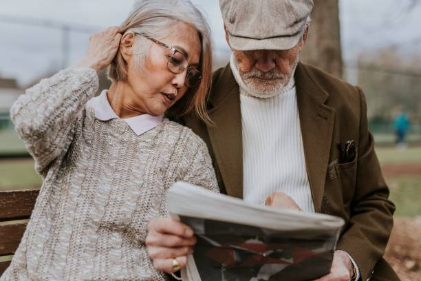 istock Couple reading newspaper on park bench 2158194887