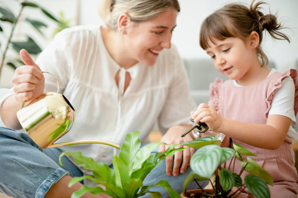 istock Kid watering potted plants with mom at home 2158197739