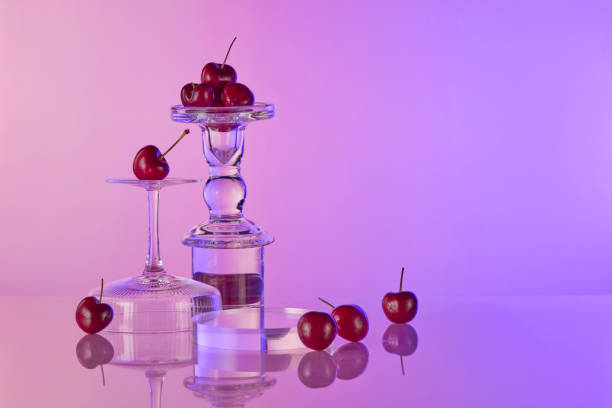 istock Purple background photo with gradient effect, on the left side placing a circular empty podium, next to a few upside down glasses and dotted with some red cherries scattered lay around 2158199276