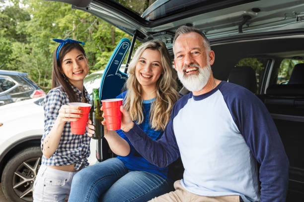 istock Friends sitting and drinking in the car boot at a tailgate party 2158204601