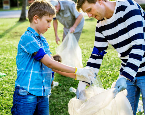 Volunteer family with three children collecting garbage and cleaning up the natural park. Concept about dedication to the cleanliness of the environment and nature.