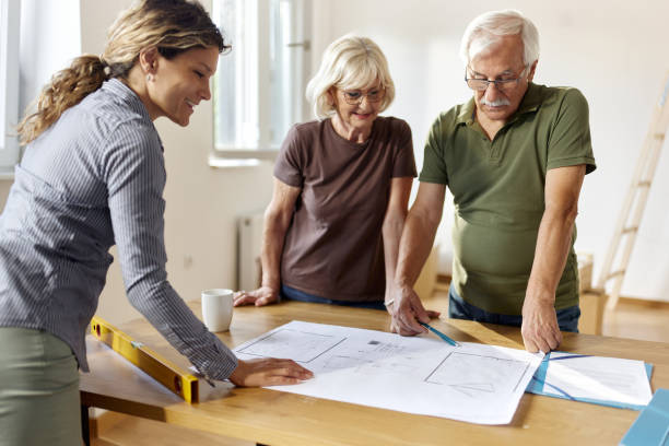 istock Senior couple analyzing blueprints with their architect at home. 2158205676