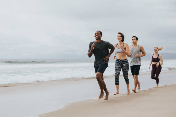 Four happy friends are jogging together on a sunny promenade by the sea, enjoying their workout and the beautiful day