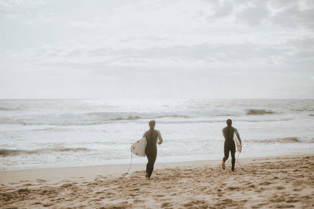 istock Surfers running on the beach 2158212574