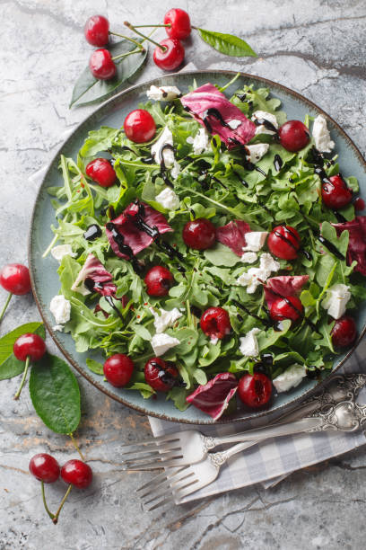 istock Summer salad with berries cherry, arugula, chicory and feta cheese dressed with balsamic sauce close-up in a plate. Vertical top view 2158215978