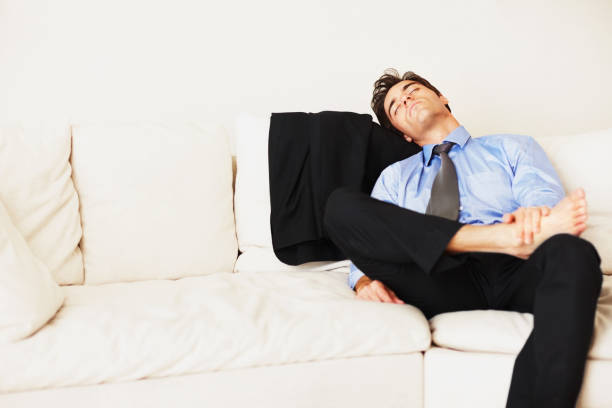 Business man sleeping on sofa in home from burnout, overworked and fatigue in living room. Tired, exhausted and sleepy entrepreneur rest for nap, break and asleep on couch to relax from low energy Young business man sleeping on couch at home tired after work stock pictures, royalty-free photos & images