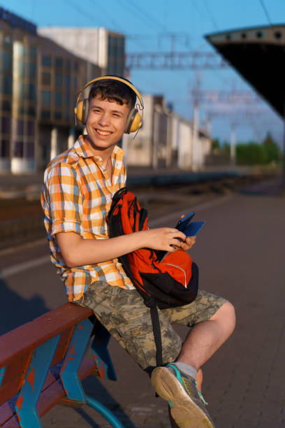 istock a student poses at a railway station, a boy on the platform is waiting for a train and listening to music with headphones, goes to study, the concept of education 2158224014