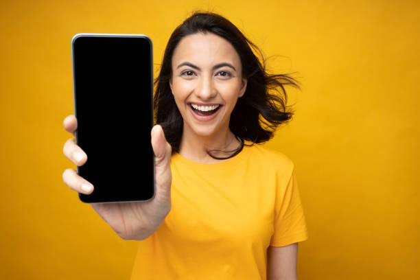 Young woman showing device screen isolate yellow background