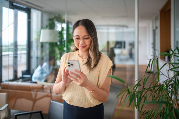 istock Asian Businesswoman Engaged with Smartphone in Office Setting 2158225569