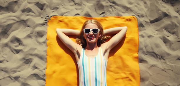 Summer vacation, happy relaxing young woman lying on sand on the beach, girl in swimsuit on towel stock photo