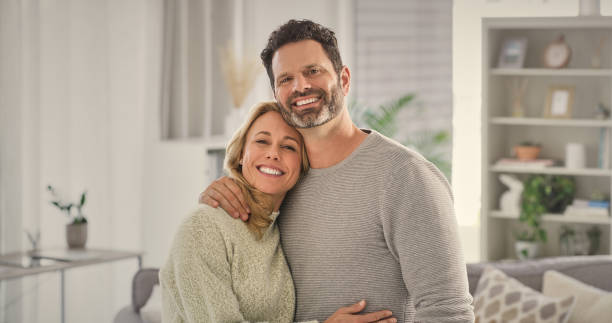 istock Portrait, couple and hug for love in house by bonding, support and marriage commitment in living room. Smile, woman and man for romance embrace, safety and loyalty with peace on anniversary together 2158229265