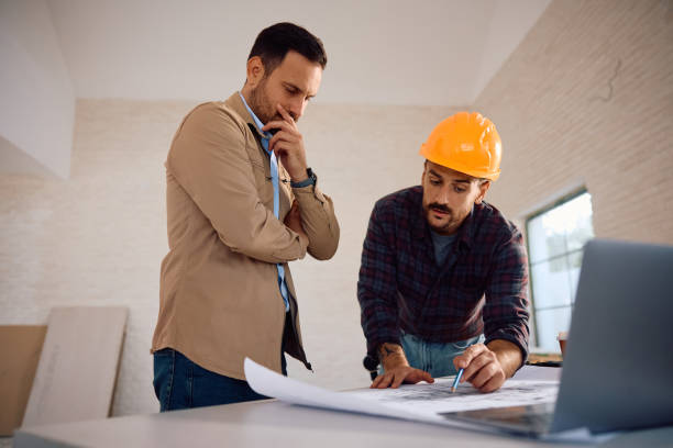 istock Pensive man analyzing housing plans with construction worker at his renovating home. 2158230739