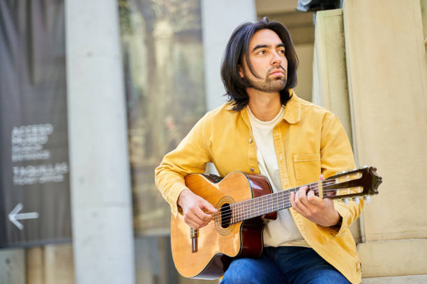 istock A man in a yellow jacket is playing a guitar. He is sitting on a ledge and he is enjoying himself 2158232294