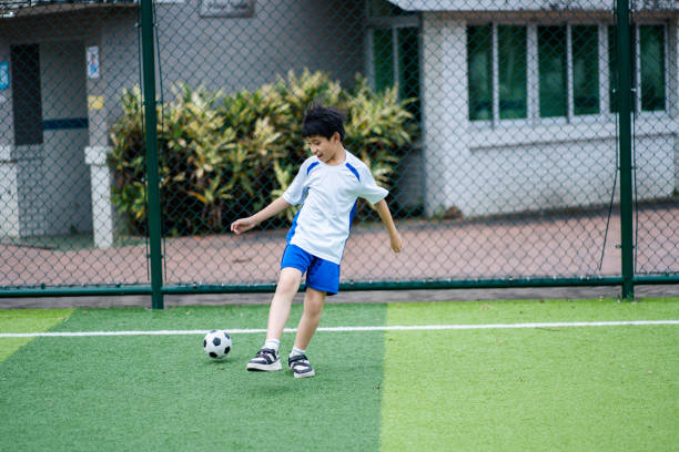 An Asian boy is playing football by himself