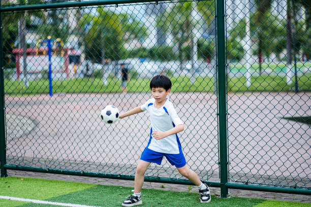 Young boy kicking a blue ball on dry grass field in a park, enjoying activity