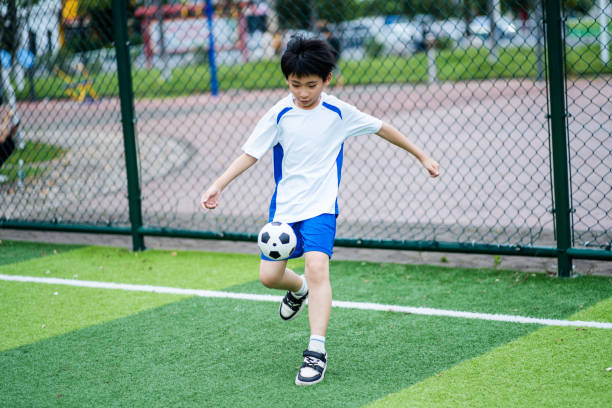 An Asian boy is playing football by himself