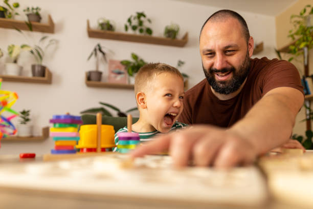 istock A father and toddler enjoying a messy game with letters. Daddy with dark hair and beard  and boy with light hair having fun. The father shows his son with his finger how to solve the task. Bonding time. Stock photo 2158240607