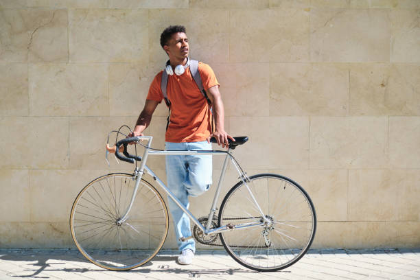 istock A student man in an orange shirt stands next to a silver bicycle 2158241346