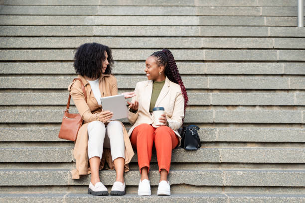 istock Two Black Businesswomen Discussing Work Outdoors With Tablet And Coffee 2158245406
