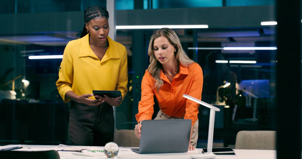 istock Overtime, team and women in office with technology, talking and discussion at night. Teamwork, late work and female partners in boardroom for strategy, corporate project and meeting together 2158245443