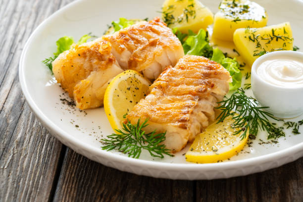 istock Fried codfish fillet and boiled potatoes served on wooden table 2158254371