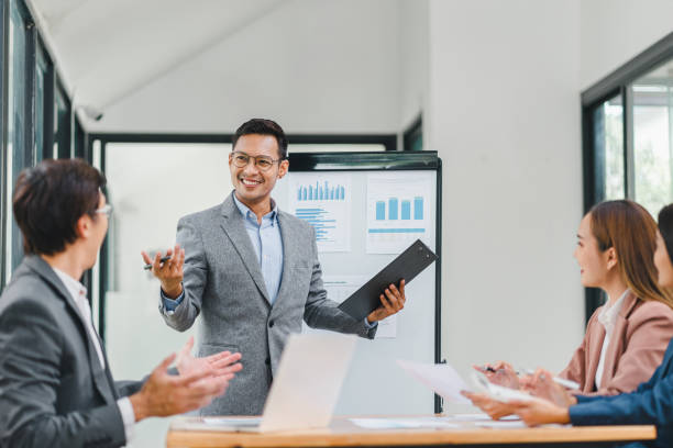 istock Confident businessman leading a meeting, engaging with colleagues while presenting data charts and graphs in a modern office. 2158254608