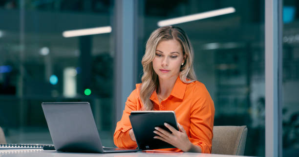 istock Laptop, tablet and woman in office reading online to apply for digital nomad for remote work. Computer, night and financial advisor with communication for email deadline on technology in workplace. 2158254621