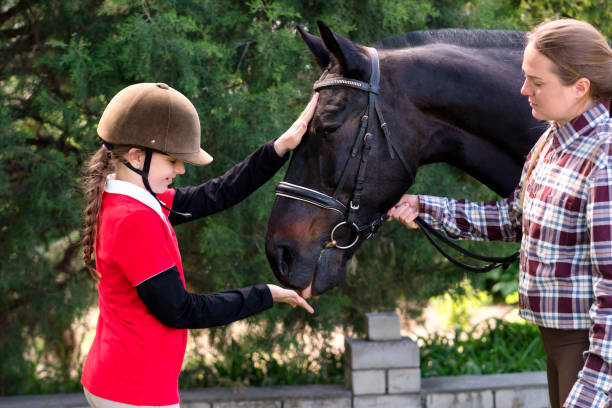 Young rider pets horse with instructor's supervision. Riding school