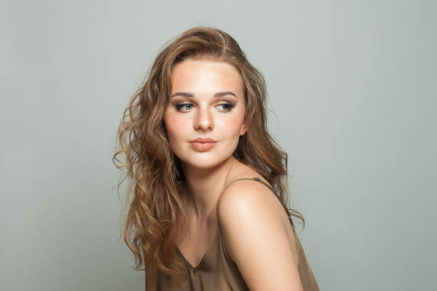 istock Young female model with make-up, clear skin and long wavy hairstyle posing on white background. Fashion beauty studio portrait of young woman 2158258237