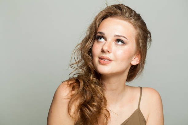 istock Looking up female model with make-up, clear skin and long wavy hairstyle posing on white background. Fashion beauty studio portrait of young woman 2158258256
