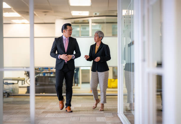 istock Two Asian business professionals walking through the office hall, engaged in conversation 2158261749