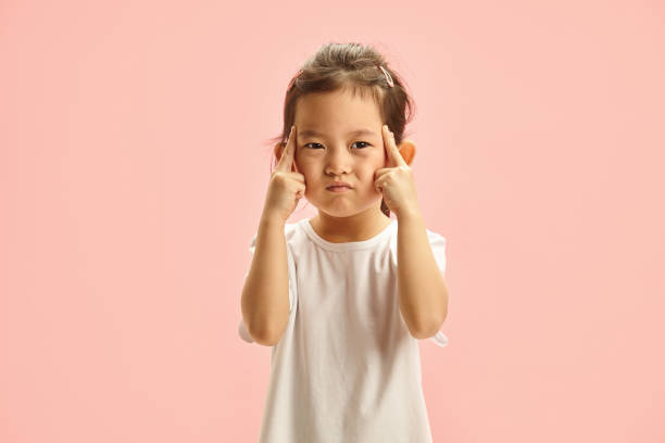 istock Pensive Child with Fingers on Temple trying remember something stands on pink isolated 2158262003
