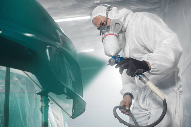 istock Car paint worker spraying green paint to car body element using spray gun in vehicle workshop chamber. Complex restoration of automobile body. 2158265689