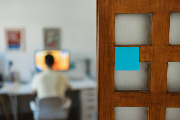 View of a workspace with a person seated at a computer desk through a door with a blue note
