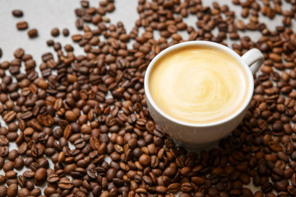 istock Freshly Brewed Cup of Latte Surrounded by Roasted Coffee Beans on Table 2158269588