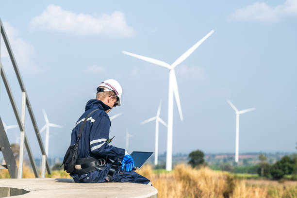istock A wind energy technician with a laptop analyzes the efficiency of turbines on a clear day. 2158270323