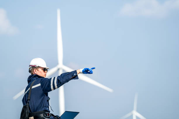 Focused engineer with a laptop conducts field analysis at a wind farm, wind turbines towering in the background.