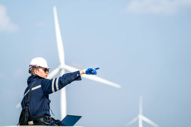 istock Focused engineer with a laptop conducts field analysis at a wind farm, wind turbines towering in the background. 2158270748