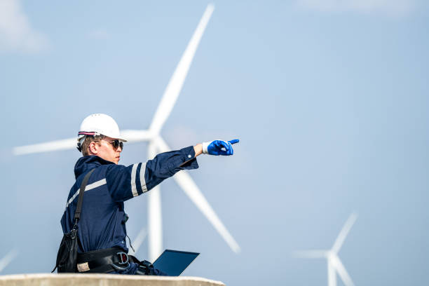 istock Focused engineer with a laptop conducts field analysis at a wind farm, wind turbines towering in the background. 2158270773