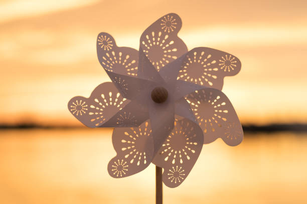Rotate white plastic pinwheel with blowing wind stands on sand by sea against smooth surface of sea bright pink sunset. Toy mill on sea beach. Large disk sun. Freedom. Lifestyle