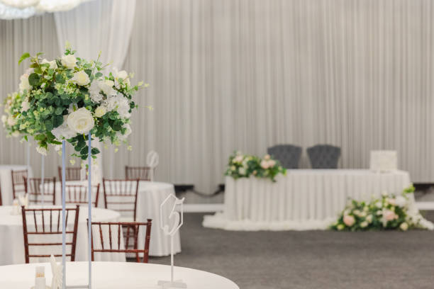 istock Decorated interior for festive event. Fancy table set for dinner with white flower composition in restaurant, luxury interior background. Wedding elegant banquet decoration arranged by catering service. 2158295103