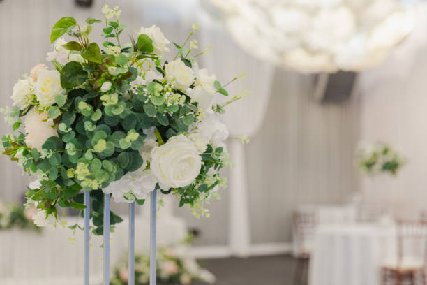 istock Decorated interior for festive event. Fancy table set for dinner with white flower composition in restaurant, luxury interior background. Wedding elegant banquet decoration arranged by catering service. 2158295556