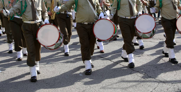 A close up of a group of uniformed drummers marching in unison down a city street, playing their drums