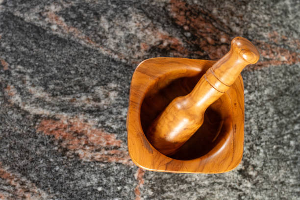A top view of a wooden mortar and pestle placed on a textured stone surface. Ideal for culinary, kitchenware, and natural cooking concepts.