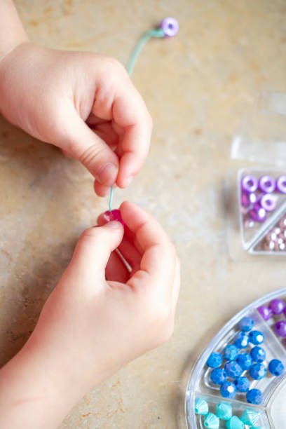 istock Preschool girl engaged in arts and crafts activity, DIY craft project, making personalized bracelet with colorful beads, fine motor skills, promoting creativity and self-expression 2158308355