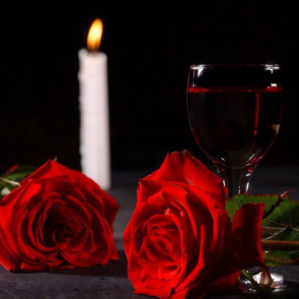 istock Intimate romantic candlelit setting, two roses, one glass of red wine, black background, can represent love, loneliness, heartbreak 2158312285