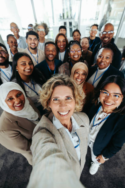 Happy company staff taking a group selfie at the office A diverse group of company staff smiling and taking a selfie at the office. Teamwork, unity, and positive corporate culture captured in one shot. workplace diversity vertical stock pictures, royalty-free photos & images
